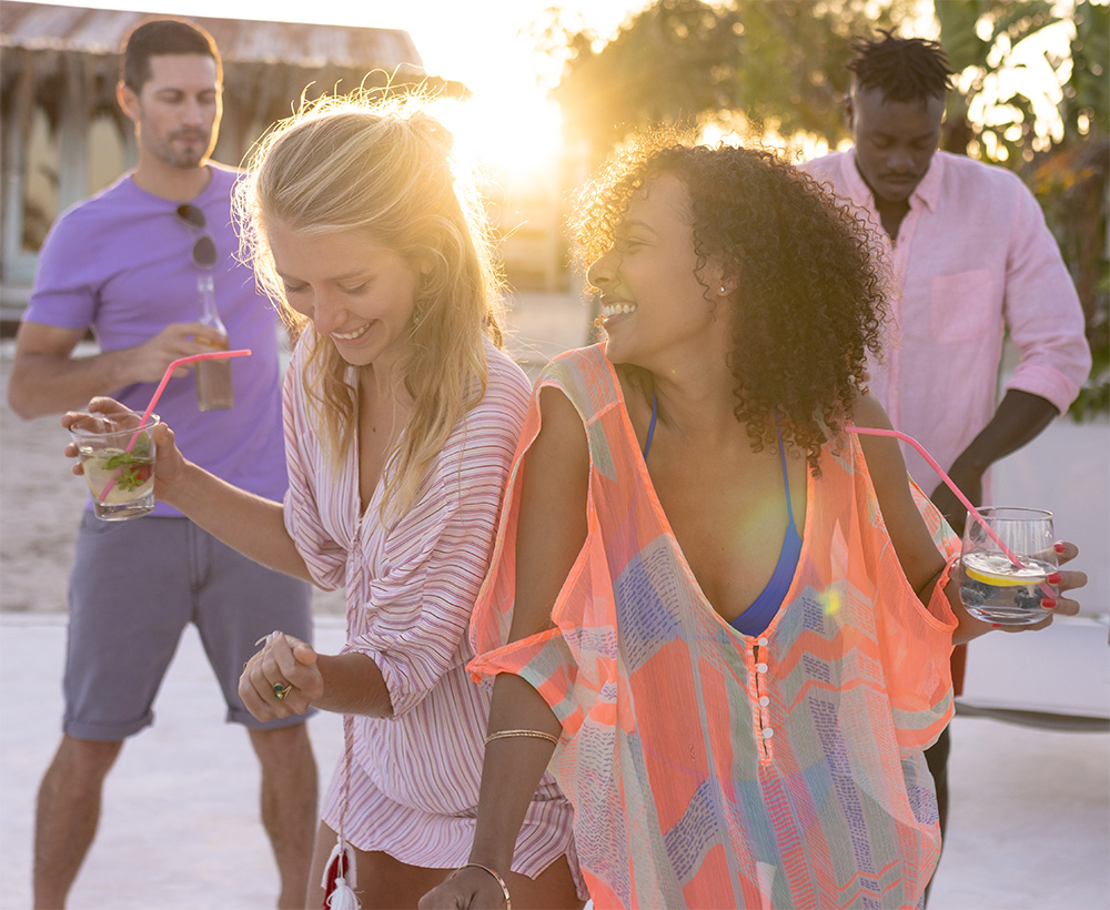 Happy group of diverse friends dancing at the resort at sunset